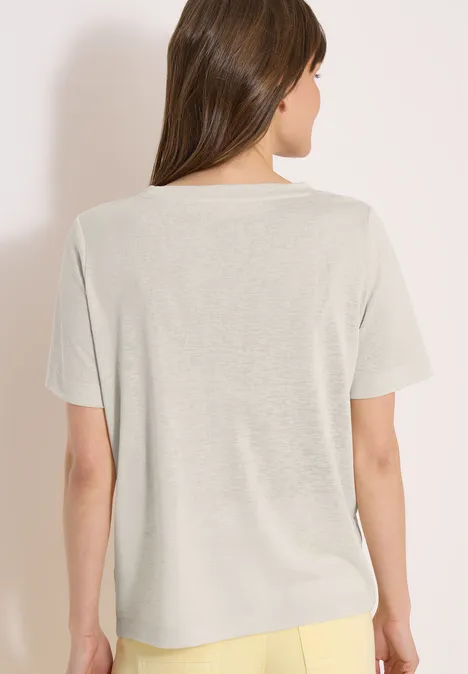 Een persoon staat met de rug naar de camera, gekleed in een beige T-shirt en gele broek voor een lichte achtergrond.