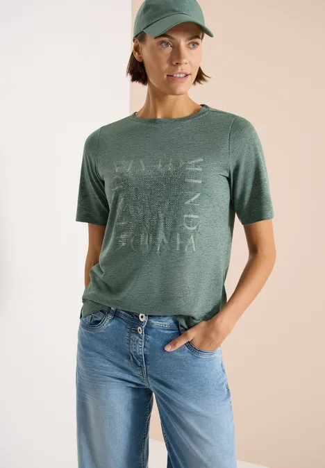 Person trägt grünes T-Shirt mit Aufdruck und lockere Jeans