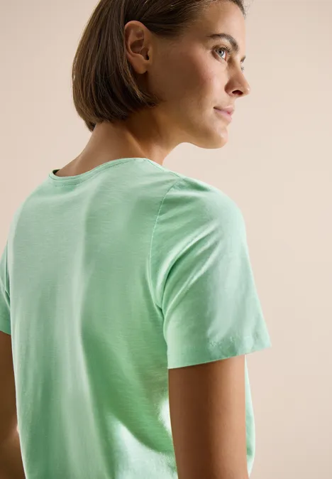 Persoon met kort haar in lichtgroen T-shirt, gezien van achteren, gezicht wazig