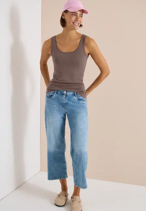 Vrouw staat in een hoek, draagt mouwloos topje, wijde cropped jeans en loafers.
