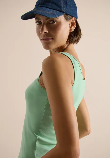 Persoon in zijaanzicht met mintgroen hemd en blauwe pet tegen neutrale achtergrond.