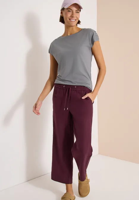 Shirt met korte mouwen en rimpels graphite light grey Persoon staat in een tweekleurige hoek, draagt een grijs t-shirt, een bordeauxrode broek en pantoffels.