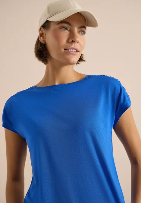 Person mit leuchtend blauem T-Shirt und Baseballcap vor neutralem Hintergrund.