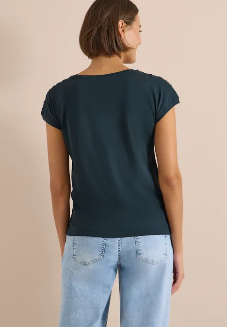 Eine Frau steht mit dem Rücken zur Kamera, trägt ein dunkelgrünes T-Shirt und hellblaue Jeans.