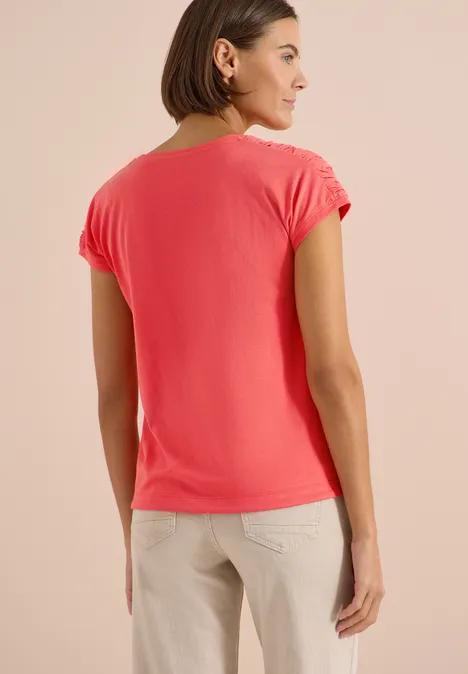 Frau von hinten in korallfarbenem T-Shirt und beigefarbenen Hosen.