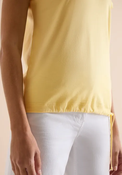 Shirt met korte mouwen en rimpels buttermilk yellow Een persoon draagt een geel mouwloos topje en witte broek, het bovenlichaam en de armen zijn zichtbaar.