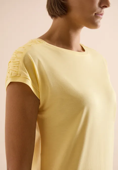 Shirt met korte mouwen en rimpels buttermilk yellow Zijaanzicht van een vrouw in een geel kort T-shirt met sierknopen op de schouders.