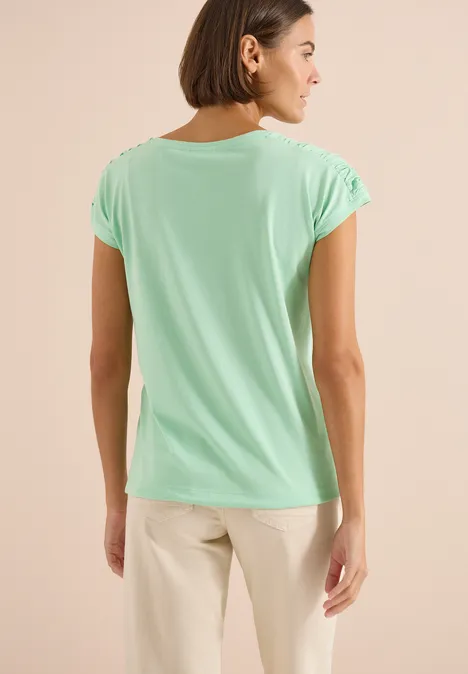 Shirt met korte mouwen en rimpels juicy lime Achteraanzicht van een vrouw in mintgroen T-shirt en lichtbeige broek voor een neutrale achtergrond.