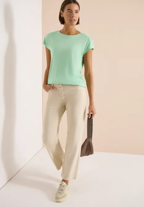 Shirt met korte mouwen en rimpels juicy lime Een vrouw draagt een mintgroen T-shirt, een wijde beige broek en een tas, staand in een lichte ruimte.