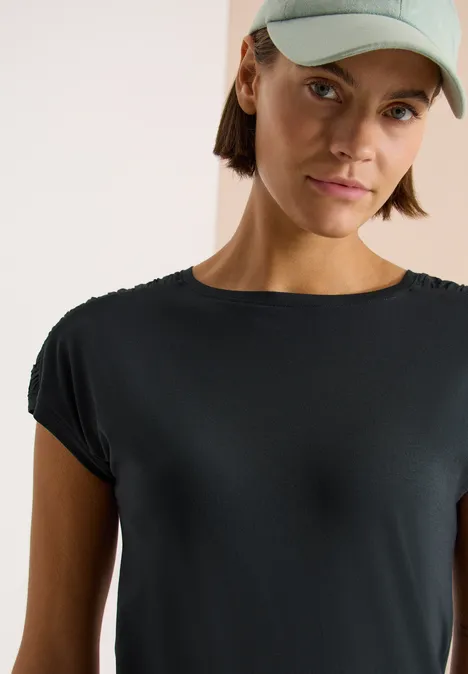 Persoon draagt zwart t-shirt en groene pet voor witte achtergrond.