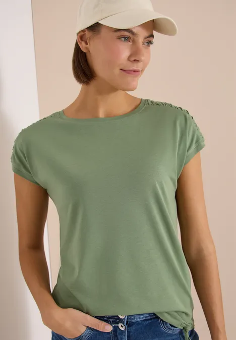 Une personne porte un t-shirt vert et une casquette blanche.