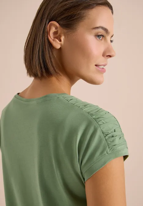 Vue de dos d'une personne en t-shirt vert avec fronces sur les manches et coupe au carré marron.