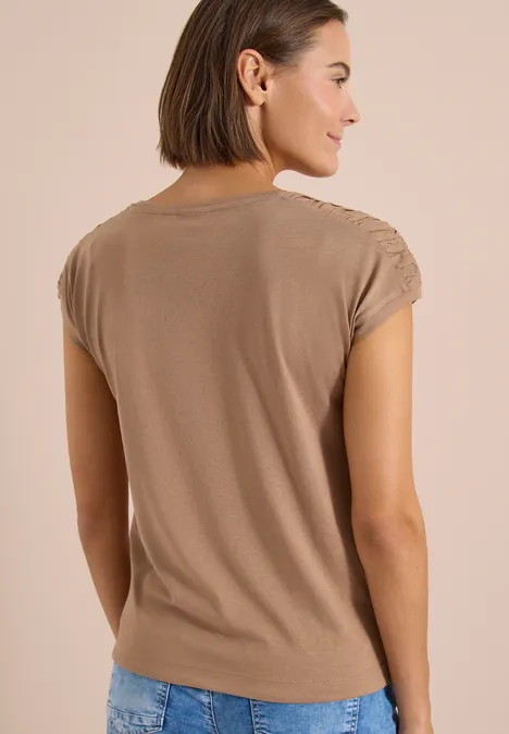 Vue de dos d’un mannequin portant un T-shirt beige à manches courtes et un jean bleu sur fond clair.