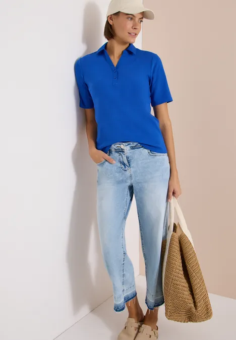 Basic Poloshirt mit Kurzarm surf blue Frau in blauem Poloshirt und hellen Jeans lehnt an Wand und hält eine Korbtasche.