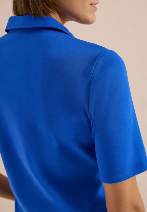 Basic Poloshirt mit Kurzarm surf blue Eine Frau mit blauem Kurzarmshirt, Rücken und Teil des Gesichts sind sichtbar.