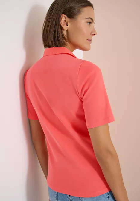 Basic Poloshirt mit Kurzarm shiny coral Rückenansicht einer Person in korallenpinken Poloshirt mit kurzen Ärmeln, die entspannt an einer Wand lehnt.