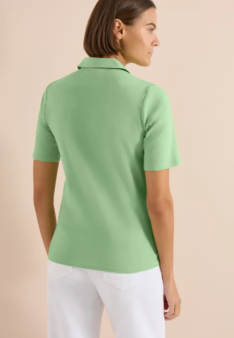 Basis polo met korte mouwen juicy lime Achteraanzicht van een vrouw in een lichtgroen poloshirt en witte broek tegen een neutrale achtergrond.
