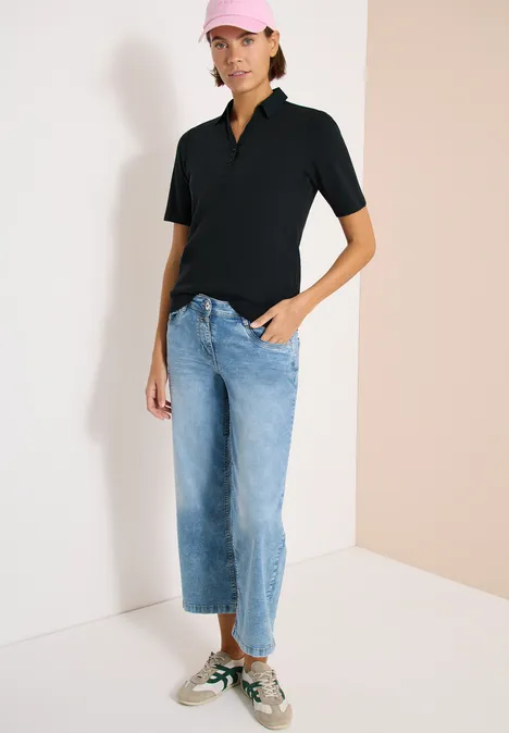 Basis polo met korte mouwen palm breeze green Persoon draagt zwart poloshirt, lichtblauwe wijde cropped jeans en groen-witte sneakers voor een tweekleurige muur.