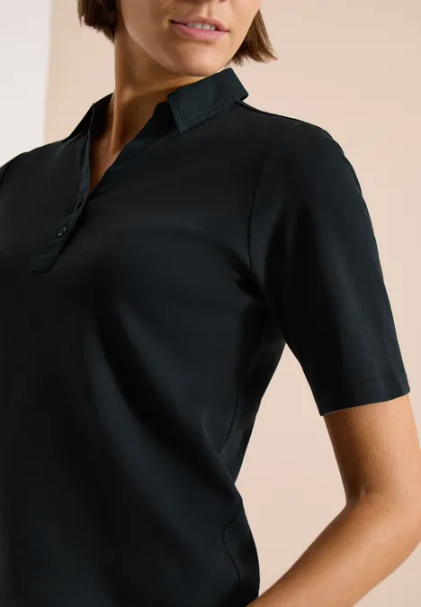 Basis polo met korte mouwen palm breeze green Een vrouw draagt een zwart poloshirt met korte mouwen en opstaande kraag.