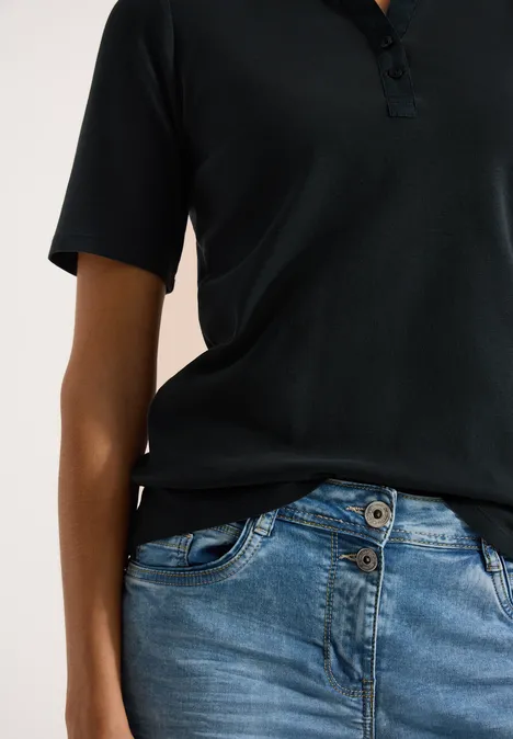 Basis polo met korte mouwen palm breeze green Zwart poloshirt en blauwe jeans, persoon van borst tot heup zichtbaar.