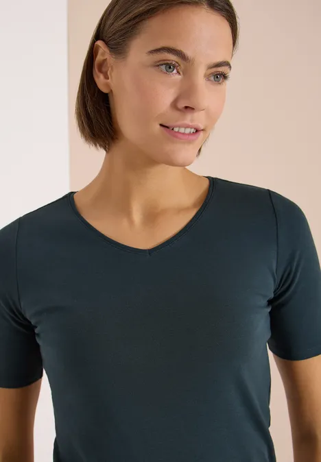 Basic T-Shirt aus Baumwolle deep petrol blue Eine Person trägt ein schlichtes, dunkelgrünes T-Shirt mit kurzen Ärmeln vor hellem Hintergrund.