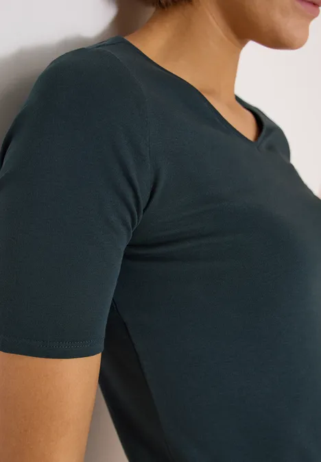 Basic T-Shirt aus Baumwolle deep petrol blue Seitliche Nahaufnahme einer Frau in einem dunkelgrünen, kurzärmligen V-Ausschnitt-Shirt.