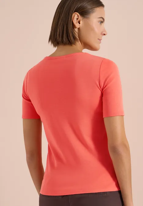 Rugaanzicht van een vrouw in een strak, koraalrood T-shirt met korte mouwen tegen een neutrale achtergrond.