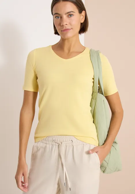 Basic katoenen shirt buttermilk yellow Vrouw in geel T-shirt en beige broek draagt groene tas over de schouder, hand in de zak.