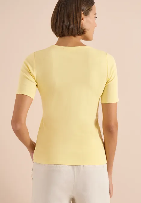 Basic katoenen shirt buttermilk yellow Rugaanzicht van een vrouw in een geel kort T-shirt en een witte broek.