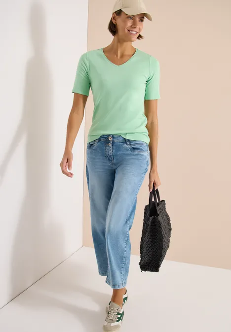 Basic katoenen shirt juicy lime Vrouw in lichtgroen T-shirt, blauwe jeans en beige pet, met zwarte tas en witte sneakers.