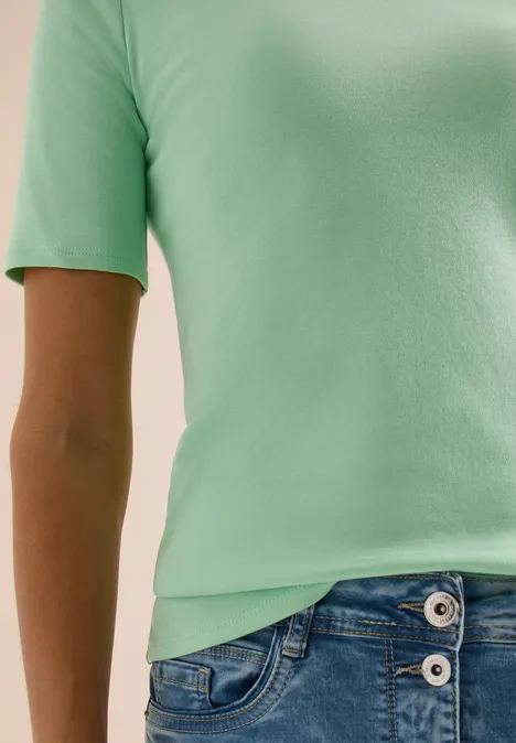 Basic katoenen shirt juicy lime Een torso met een mintgroen T-shirt en blauwe spijkerbroek met knopen, arm zijdelings zichtbaar.