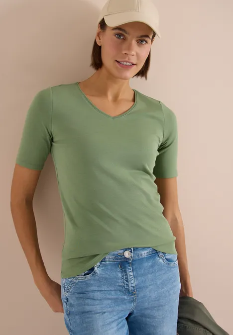 T-shirt basique en coton deep matcha green Femme en t-shirt vert et jean bleu, coiffée d'une casquette, tenant une veste