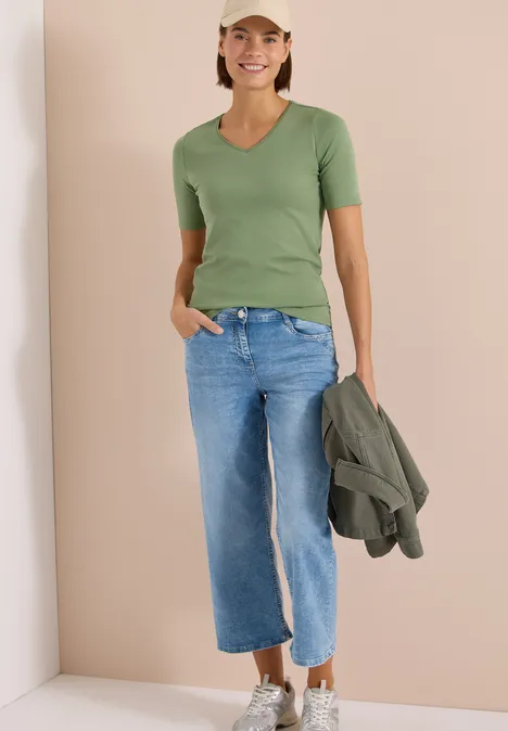 T-shirt basique en coton deep matcha green Personne sur fond beige portant un T-shirt vert, un jean large bleu et tenant une veste verte.