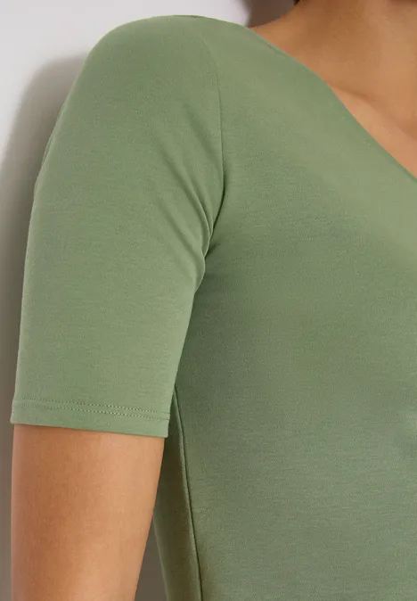 T-shirt basique en coton deep matcha green Vue latérale d'une personne portant un haut vert moulant à manches courtes sur fond blanc.