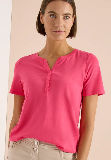 Vrouw in een roze T-shirt met korte mouwen tegen neutrale achtergrond.