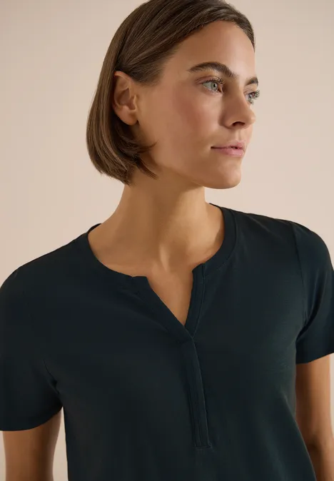 Oberkörper einer Person mit unscharfem Gesicht, kurzen Haaren und dunkelblauem Henley-Shirt vor hellem Hintergrund.