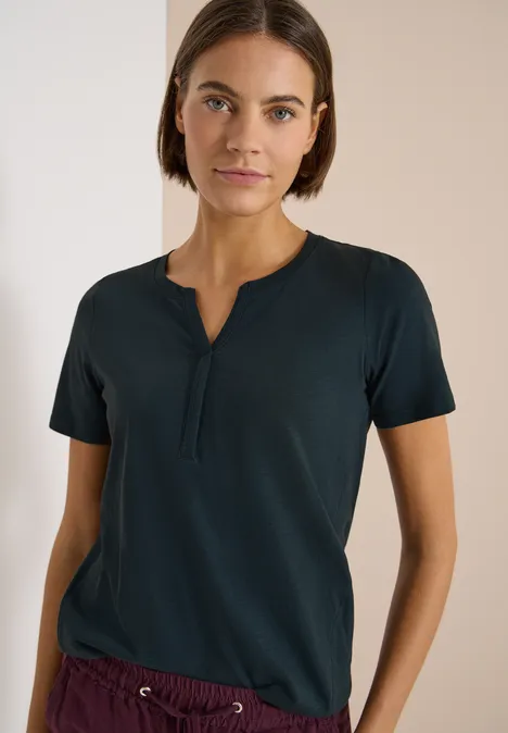 Frau trägt ein schlichtes dunkelgrünes Kurzarmshirt mit kleinem Schlitz am Rundhalsausschnitt.