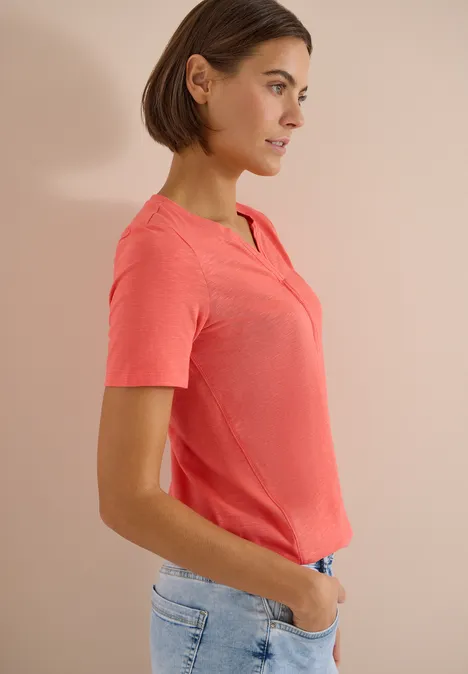 Frau in rosa T-Shirt und Jeans, seitlich, Hände in den Taschen.