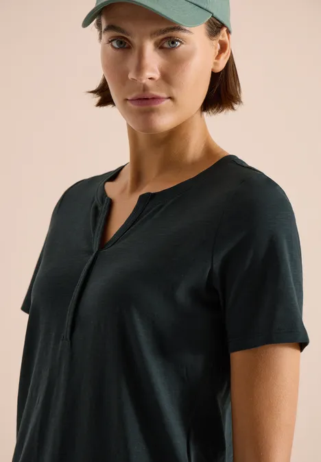 Basic shirt in tuniekstijl palm breeze green Persoon draagt een donkerblauw T-shirt met korte mouwen en Henley-hals, en een groene pet.