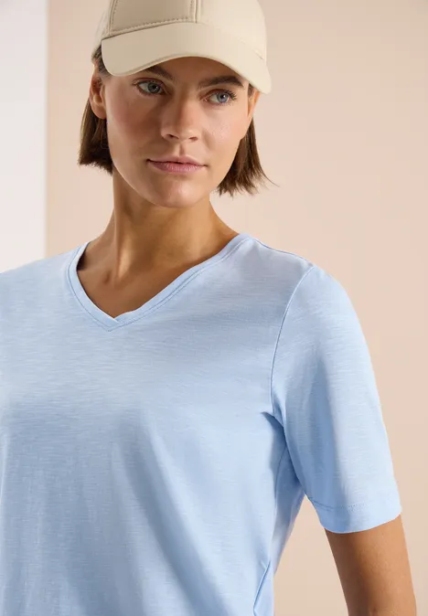 Basic Shirt met V-hals light sky blue Een persoon draagt een lichtblauw V-hals T-shirt met korte mouwen tegen een vage achtergrond.