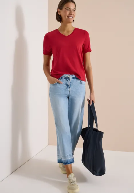 Basic T-Shirt mit Kurzarm und V-Neck tamarillo red Eine Person mit rotem T-Shirt, hellblauen Jeans, weißen Sneakern und dunkelblauer Tasche vor hellem Hintergrund.
