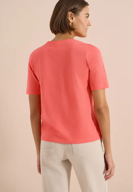 Basic T-Shirt mit Kurzarm und V-Neck shiny coral Frau von hinten in korallfarbenem T-Shirt und beige Hose vor hellem Hintergrund