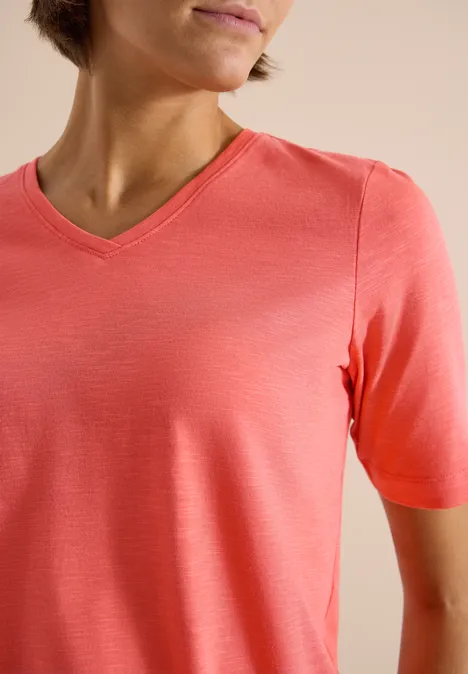 Basic T-Shirt mit Kurzarm und V-Neck shiny coral Person trägt ein korallenfarbenes V-Ausschnitt-Shirt vor neutralem Hintergrund.
