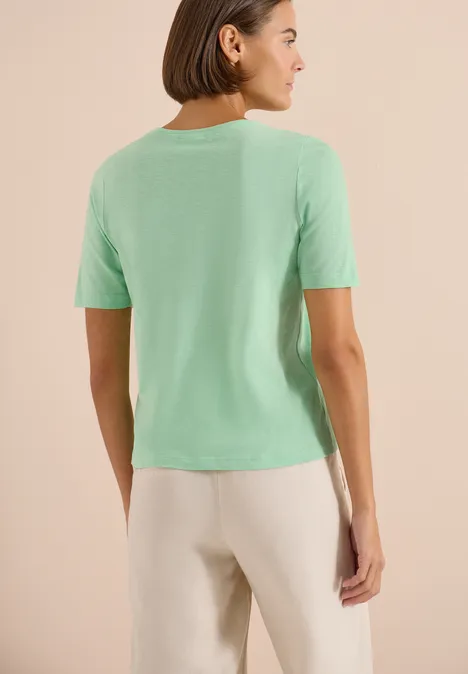Basic Shirt met V-hals juicy lime Vrouw van achter gezien in een mintgroen T-shirt en beige broek.