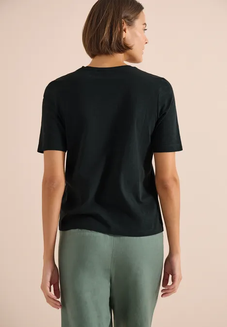 Basic Shirt met V-hals palm breeze green Vrouw van achteren in een zwart t-shirt en groene broek tegen neutrale achtergrond