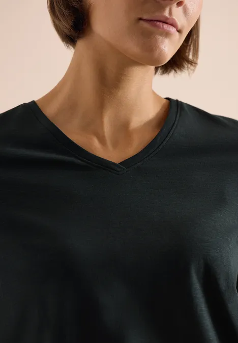 Basic Shirt met V-hals palm breeze green Close-up van persoon met donker V-hals T-shirt, alleen kin, hals en borst zichtbaar.