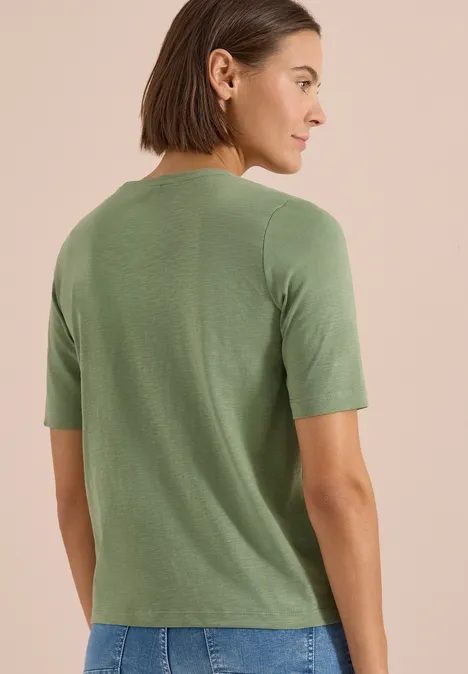 Kobieta od tyłu w khaki T-shircie z krótkim rękawem na neutralnym tle.