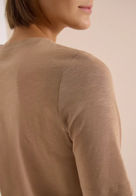Frau im beigen Langarmshirt, von hinten fotografiert, der Kopf leicht nach rechts gedreht.