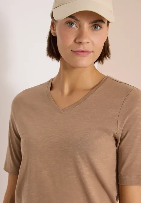 Eine Person trägt ein schlichtes beigefarbenes T-Shirt mit V-Ausschnitt.