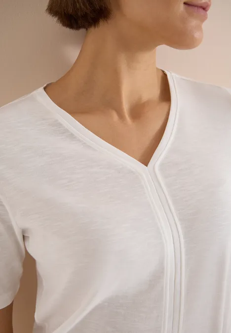 Une femme porte un t-shirt blanc à col en V, vue du cou à la poitrine.
